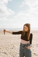 mulher bonita com cabelo comprido, loira tira foto no celular na praia no verão