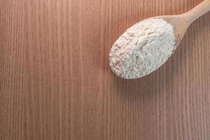 colher de pau com farinha de trigo na mesa de madeira foto