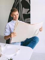 homem adolescente moderno lendo jornal de papel durante o café da manhã em casa. leitura, moda antiga, moderna, conceito de notícias foto