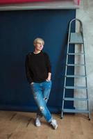 jovem loira moderna em moletom preto e jeans em pé perto de escada e planejamento de renovação foto