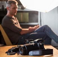 câmera e equipamento em cima da mesa no estúdio no fundo do fotógrafo sentado foto