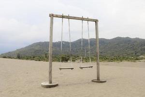 o velho balanço de madeira de corda no deserto ou praia arenosa com fundo de montanha foto