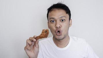 choque e uau cara de jovem asiático está comendo frango frito vestindo camisa branca. foto