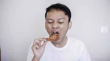 jovem asiático está comendo frango frito, use camisa branca foto