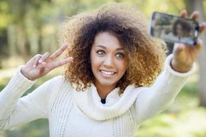 jovem garota afro-americana selfie no parque com um smartphone foto