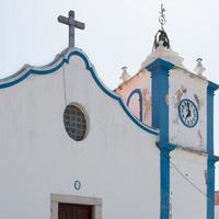 close-up de uma antiga igreja com torre do relógio e cruz católica. alentejano, portugal foto