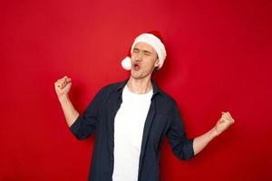 retrato de homem louco engraçado comemorar a vitória levantar os punhos gritar sim usar chapéu de Natal, camisa azul isolada sobre o espaço de fundo de cor vermelha para texto. conceito - ótimas notícias, fortuna, pessoas, ano novo foto