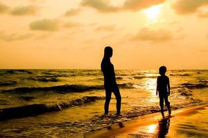silhueta de jovem e menino andando na praia foto