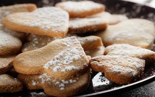 deliciosos biscoitos caseiros em forma de coração polvilhados com açúcar de confeiteiro em pano de saco e tábuas de madeira. imagem horizontal vista contra a luz de fundo. foto