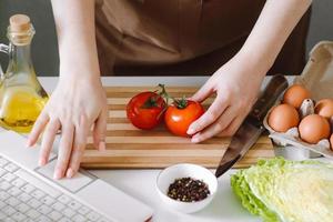 blogueira de mulher preparando salada de vegetais de dieta. aulas de culinária online, usando um laptop na cozinha. foto