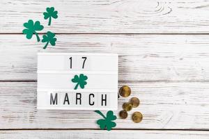 flatlay para st. dia de patrício. moedas de ouro e folhas de trevo em um fundo branco de madeira. feliz feriado irlandês, símbolos de sorte. foto