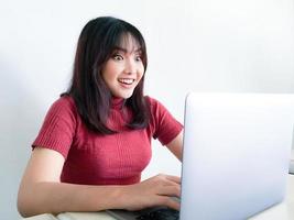 mulher asiática usa camisa vermelha com laptop sentindo gritos animados com alegria e felicidade, surpresa, expressão vencedora, fundo branco. mulheres indonésias foto