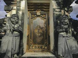 porta ou portão para entrar no detalhe da arquitetura tradicional do jardim balinês. portão de madeira indonésio guardado por estátuas de pedra. foto