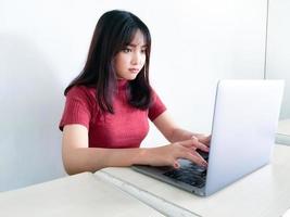 menina bonita asiática séria ou pensando na frente do laptop no fundo branco isolado foto