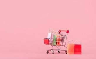 conceito de compras. caixas ou caixas de papel e sacola de compras no carrinho de compras vermelho sobre fundo rosa. consumidores de compras on-line podem fazer compras em casa e serviço de entrega foto