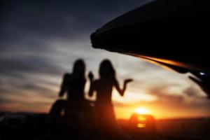 duas garotas felizes em posar ao lado de um carro preto foto