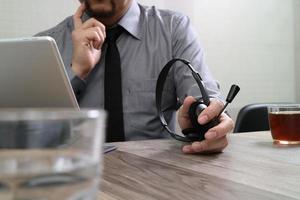 homem de negócios usando fone de ouvido voip com teclado inteligente de encaixe de computador tablet digital, comunicação de conceito, suporte, na mesa de madeira foto