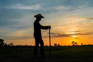 fazendeiro segurando uma enxada em um campo ao pôr do sol foto