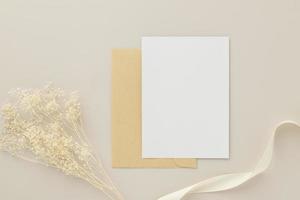 maquete de convite de cartão em branco 5x7 em envelope marrom com flores secas em fundo bege, postura plana, maquete foto