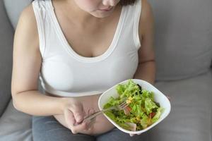 jovem grávida comendo salada em casa, cuidados de saúde e gravidez foto