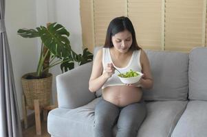 jovem grávida comendo salada em casa, cuidados de saúde e gravidez foto