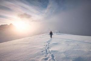 alpinista de homem andando com pegada de neve no cume do pico foto