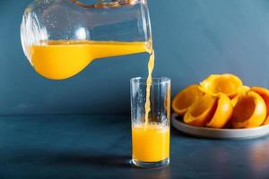 uma mão anônima está enchendo o copo de suco de laranja fresco foto