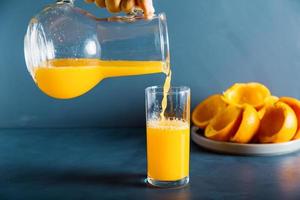 uma mão anônima está enchendo o copo de suco de laranja fresco foto