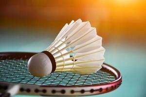 peteca de badminton branca creme e raquete com sombreamento de luz neon no chão verde na quadra de badminton indoor, fundo de badminton desfocado, espaço de cópia. foto