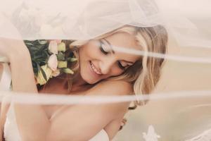 retrato de uma noiva loira linda com um buquê de flores com penteado e maquiagem de casamento. noiva de luxo com véu sobre o rosto. closeup retrato da jovem noiva linda. Casamento. espaço de cópia foto