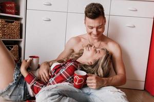 linda garota sentada no chão e se divertindo com o namorado. jovem casal desfrutando de café ou chá na cozinha. foto