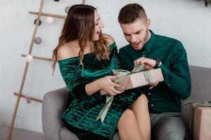 abrindo o presente de natal. casal apaixonado feliz aproveite a celebração do feriado de natal. casal amoroso abraço sorrindo enquanto desembalar presente árvore de natal background.what uma surpresa. foto