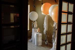 decoração para primeiro aniversário com bolo de dois andares e grandes balões brancos e bege com enfeites. barra de chocolate com biscoito ou macarons. festa de aniversário. foco seletivo foto