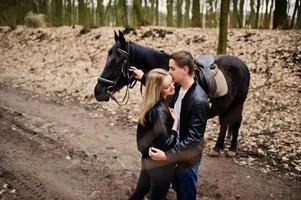 jovem casal elegante apaixonado perto de cavalo na floresta de outono. foto