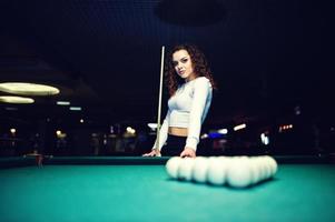 jovem encaracolada posou perto da mesa de bilhar. modelo sexy na minissaia preta jogar sinuca russa. jogar jogo e conceito divertido. foto