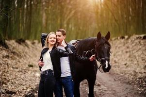 jovem casal elegante apaixonado perto de cavalo na floresta de outono. foto