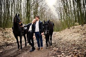 jovem casal elegante apaixonado perto de cavalos na floresta de outono. foto