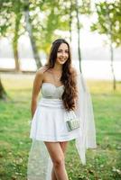 retrato de menina morena vestindo vestido branco com bolsa contra o parque na festa de despedida. foto