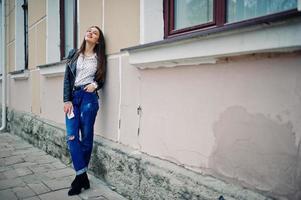 retrato de jovem elegante usar jaqueta de couro e jeans rasgados com telefone celular na mão. estilo de modelo de moda de rua. foto