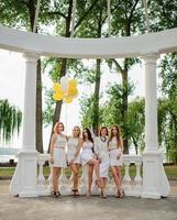 cinco meninas com balões na mão usavam vestidos brancos na festa de despedida contra colunas brancas de arco. foto