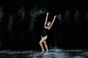 dançarina pulando e dançando na poeira branca com farinha em um fundo preto. tiro de estúdio de mulher dançando com farinha. foto