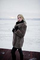 retrato de jovem elegância loira com um casaco de pele no rio nevoento de fundo cais no gelo de inverno. foto