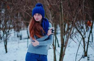 retrato de uma jovem ruiva com sardas vestindo chapéu de lã de malha azul e cachecol com uma xícara de chá em dia de inverno. foto