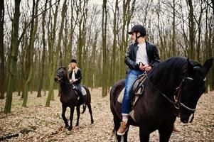 jovem casal elegante montando cavalos na floresta de outono. foto