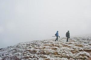 dois fotógrafos turísticos com tripé na mão andando na colina congelada com neblina. foto