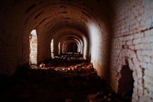 túnel de arco de tijolo assustador no escuro e um pouco de luz. foto