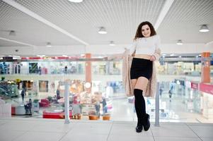 menina jovem modelo encaracolado posou na mini-saia no grande centro comercial perto de grades de vidro. foto