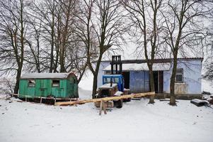 trator soviético velho enferrujado coberto de neve contra a cabine de trabalho. foto