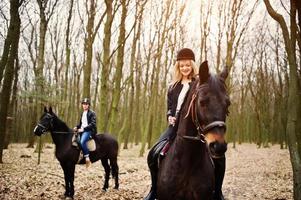 jovem casal elegante montando cavalos na floresta de outono. foto