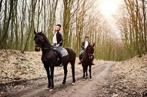 jovem casal elegante montando cavalos na floresta de outono. foto